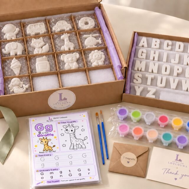 The A–Z Alphabet Kit unpacked: gypsum shapes in a divided box, the gypsum letters A to Z in a tray, a G is for Giraffe activity card, two paintbrushes, two strips of paint pots, a packet of magnets and a thank-you card